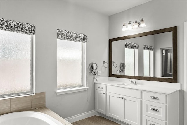 bathroom with a bathing tub, vanity, baseboards, and wood finished floors