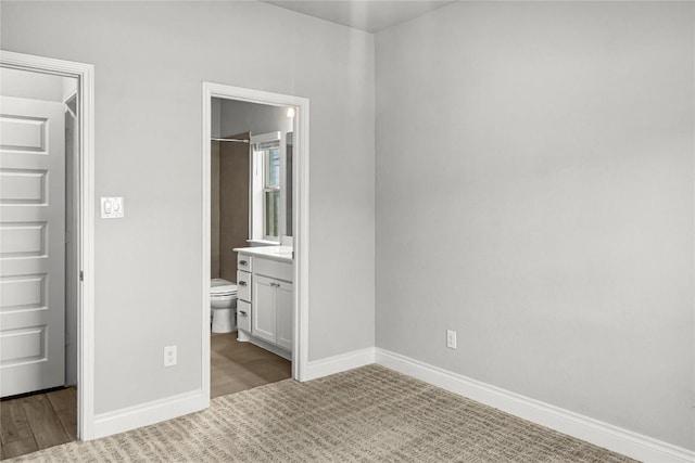 unfurnished bedroom with carpet flooring, baseboards, and connected bathroom