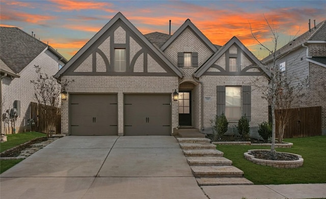 view of front of property featuring driveway, an attached garage, fence, a yard, and brick siding