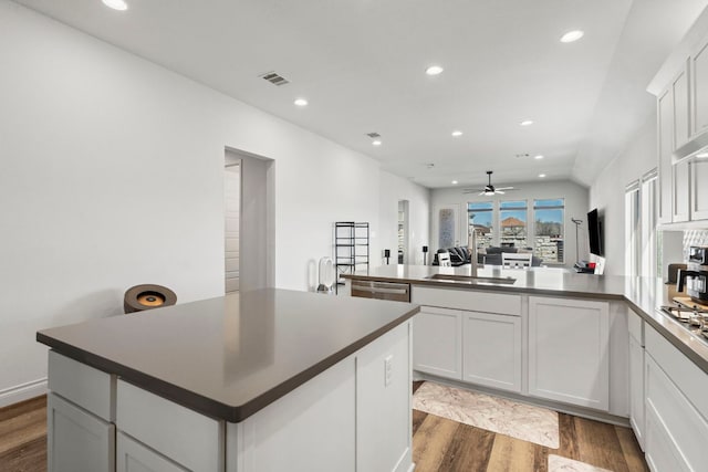 kitchen with dark countertops, visible vents, dark wood finished floors, a peninsula, and a sink