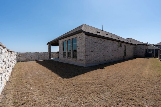 view of side of home with a yard, central AC, a fenced backyard, and brick siding