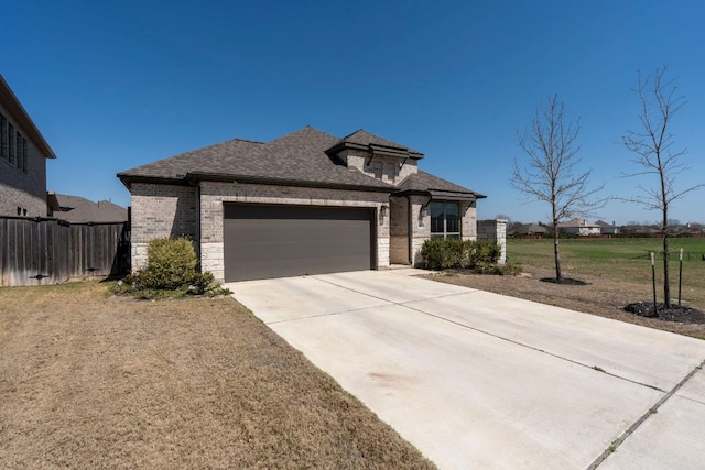 view of front of home featuring driveway, fence, roof with shingles, an attached garage, and brick siding