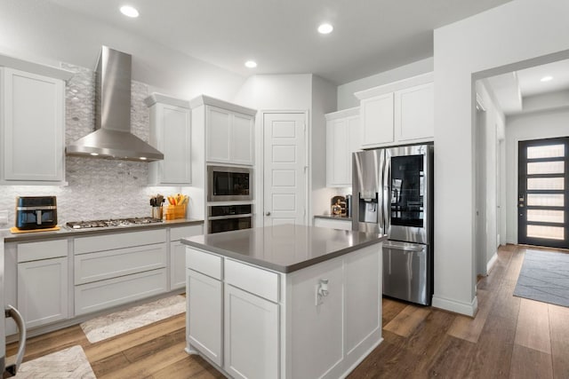 kitchen with wood finished floors, stainless steel appliances, decorative backsplash, wall chimney range hood, and a center island