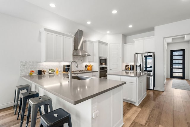 kitchen featuring a sink, a kitchen island, stainless steel appliances, light wood-style floors, and wall chimney exhaust hood