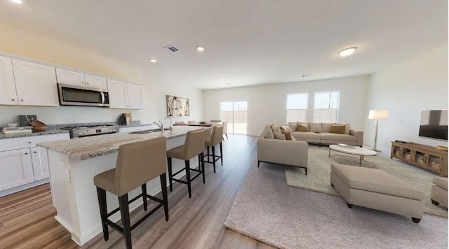 kitchen featuring visible vents, open floor plan, a breakfast bar area, stainless steel appliances, and white cabinetry