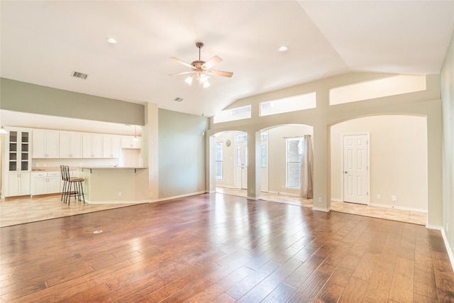 unfurnished living room with arched walkways, a ceiling fan, visible vents, wood finished floors, and baseboards