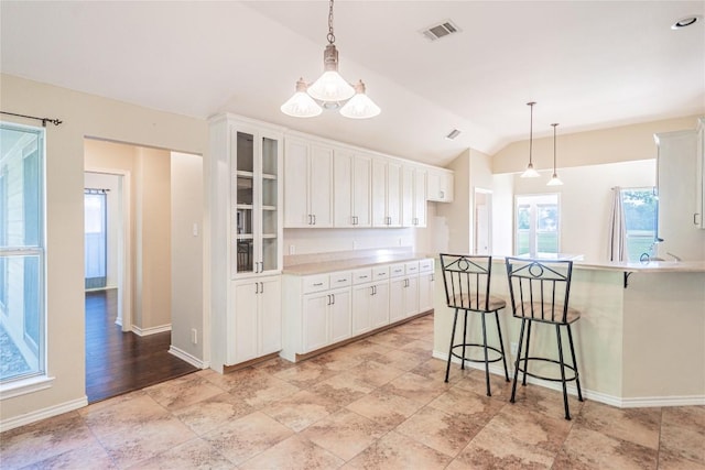 kitchen with glass insert cabinets, a kitchen bar, vaulted ceiling, visible vents, and white cabinets