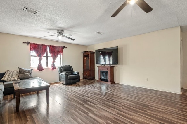 living room with a glass covered fireplace, wood finished floors, visible vents, and a ceiling fan