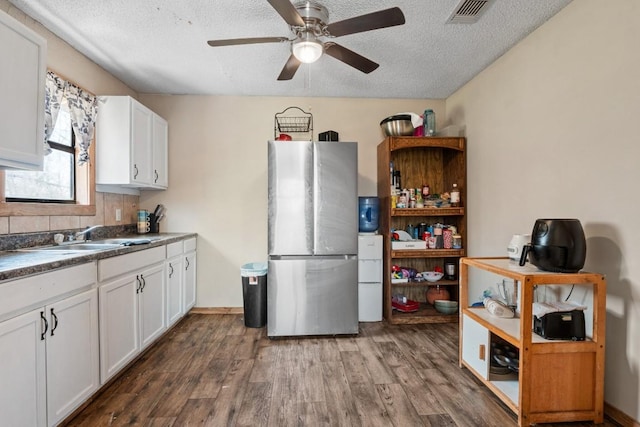 kitchen with a sink, a textured ceiling, wood finished floors, freestanding refrigerator, and white cabinets