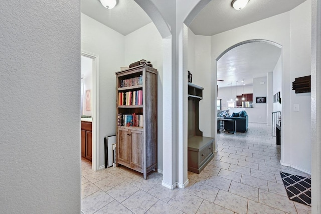 corridor featuring arched walkways, light tile patterned floors, baseboards, and a textured wall