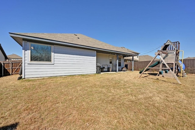 back of property with a fenced backyard, a yard, and a playground