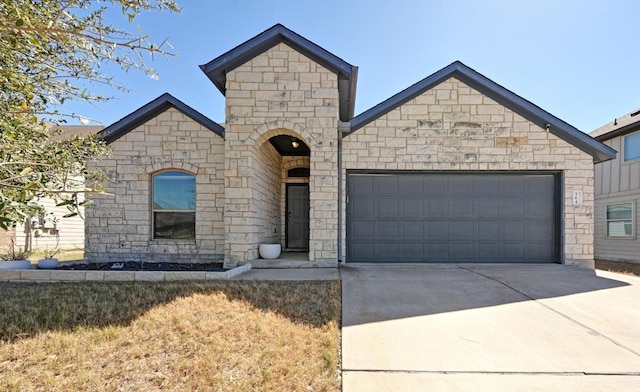 french country home featuring an attached garage, stone siding, and concrete driveway