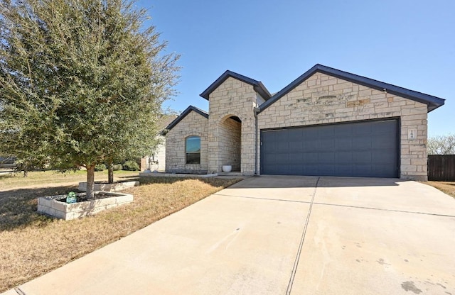 french country inspired facade with stone siding, driveway, and a garage