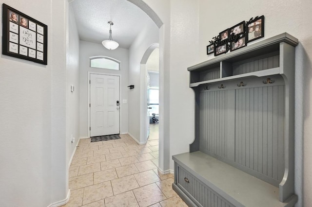 mudroom featuring light tile patterned floors, baseboards, arched walkways, and a textured ceiling