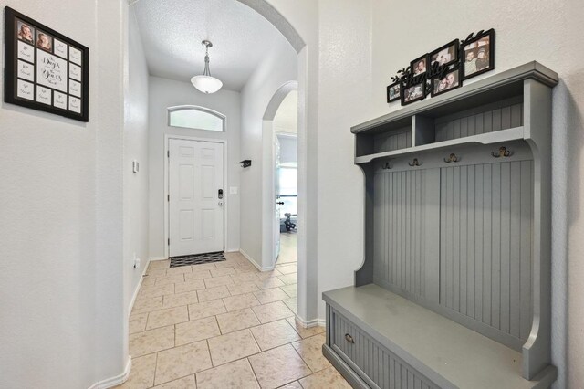 mudroom featuring arched walkways, light tile patterned flooring, a textured ceiling, and baseboards