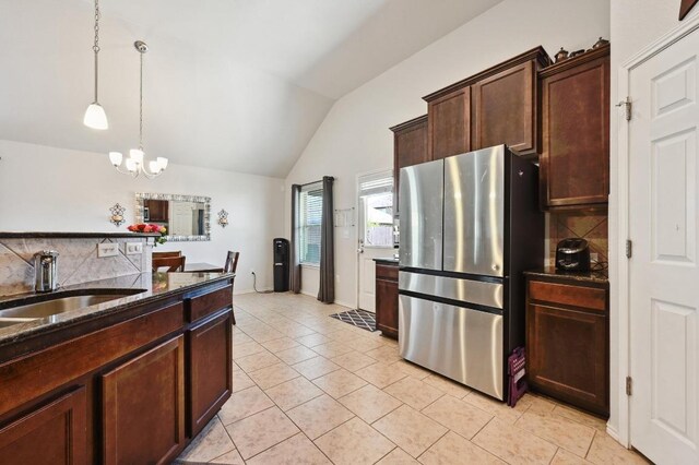 kitchen with a sink, decorative light fixtures, dark stone countertops, freestanding refrigerator, and lofted ceiling