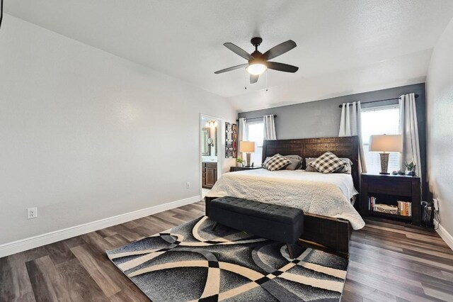 bedroom with dark wood finished floors, vaulted ceiling, connected bathroom, baseboards, and ceiling fan