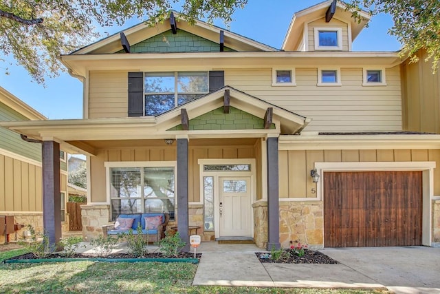 craftsman-style home featuring driveway, stone siding, covered porch, board and batten siding, and a garage