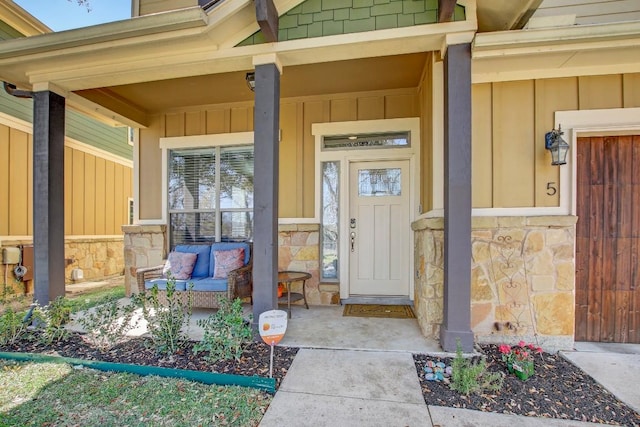 view of exterior entry featuring stone siding, covered porch, and board and batten siding