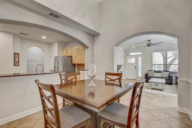 dining room featuring light tile patterned floors, baseboards, visible vents, arched walkways, and ceiling fan