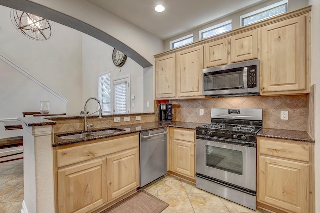 kitchen with a sink, a peninsula, light brown cabinets, and stainless steel appliances