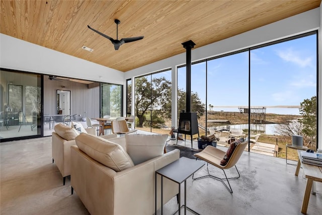 sunroom featuring visible vents, lofted ceiling, wooden ceiling, a wood stove, and a ceiling fan