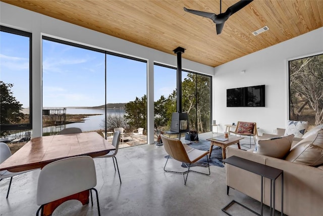 sunroom featuring visible vents, a water view, a ceiling fan, wood ceiling, and a wood stove