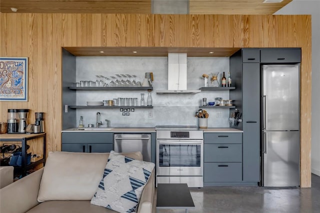 kitchen featuring gray cabinetry, open shelves, a sink, stainless steel appliances, and wall chimney exhaust hood