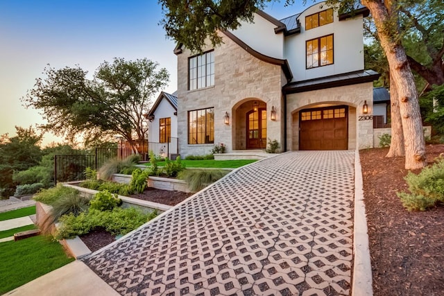 view of front of home featuring stucco siding, stone siding, an attached garage, and driveway