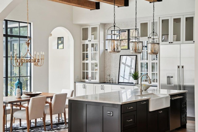 kitchen featuring a center island with sink, dark cabinetry, arched walkways, white cabinetry, and a sink