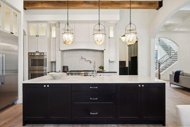 kitchen featuring backsplash, beam ceiling, appliances with stainless steel finishes, dark cabinetry, and white cabinetry