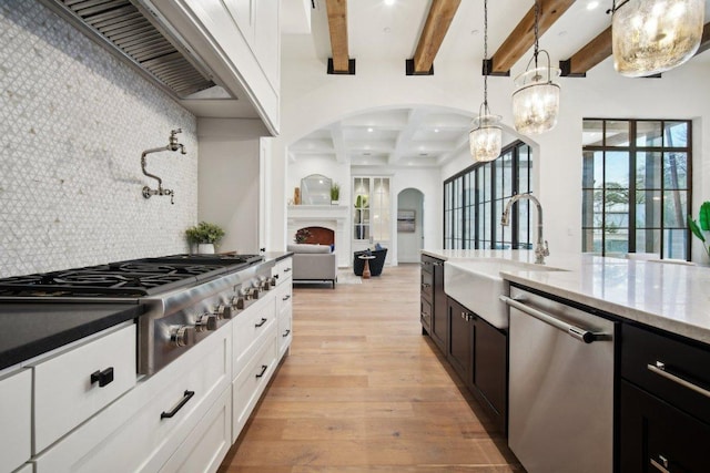 kitchen featuring a sink, stainless steel appliances, exhaust hood, light wood finished floors, and decorative backsplash