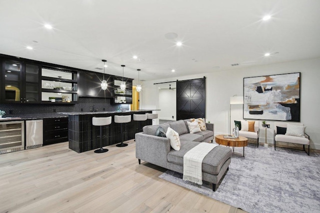 living room featuring recessed lighting, a barn door, wine cooler, light wood finished floors, and wet bar