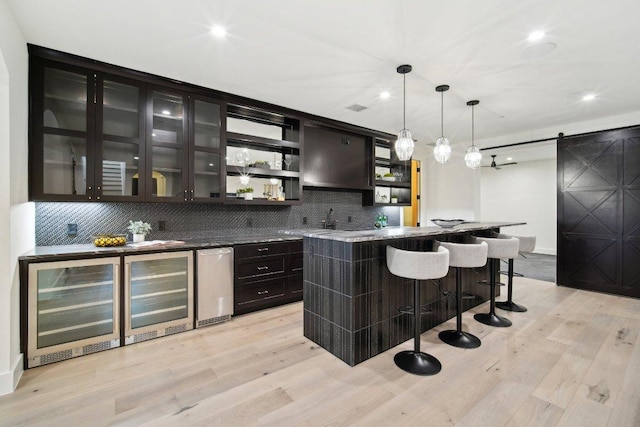 bar featuring wet bar, pendant lighting, a barn door, light wood-type flooring, and backsplash