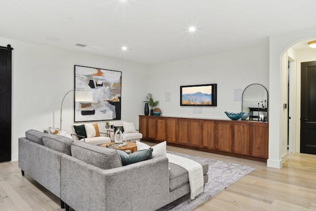 living room featuring a barn door, recessed lighting, arched walkways, and light wood finished floors