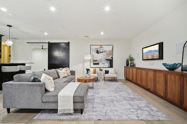 living room with a barn door, recessed lighting, and light wood finished floors