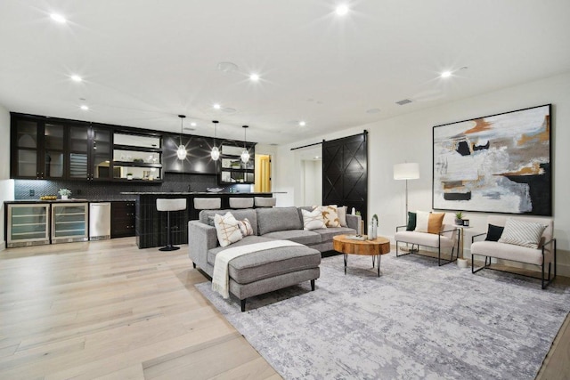 living area featuring wine cooler, light wood-style flooring, a bar, and a barn door