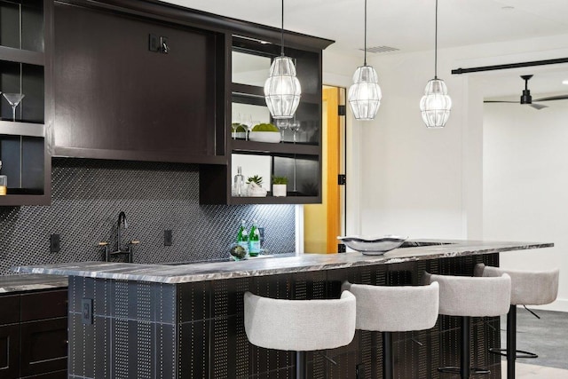 kitchen with a ceiling fan, visible vents, pendant lighting, a kitchen bar, and backsplash