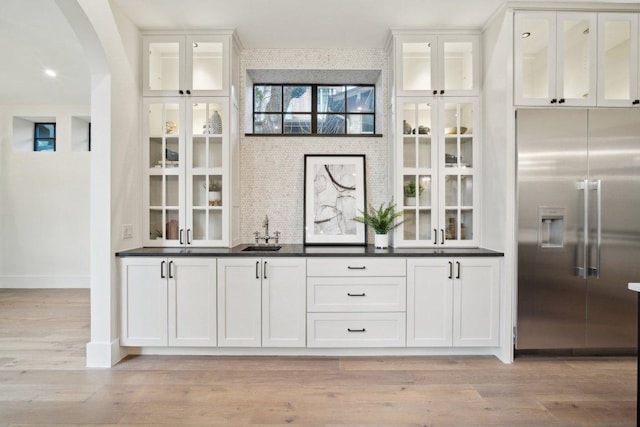 bar featuring stainless steel built in refrigerator, light wood-style flooring, arched walkways, and a sink