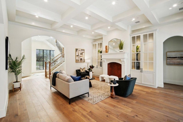 living room with stairway, beam ceiling, a fireplace, light wood-style floors, and coffered ceiling