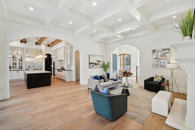 living room featuring beamed ceiling, baseboards, arched walkways, and light wood finished floors