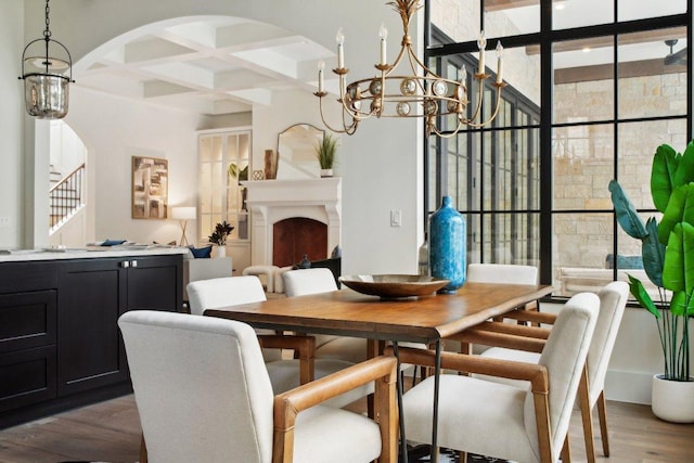 dining space with beamed ceiling, coffered ceiling, wood finished floors, arched walkways, and a chandelier