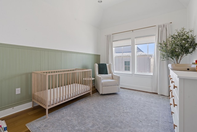 bedroom with a nursery area, wood finished floors, and wainscoting