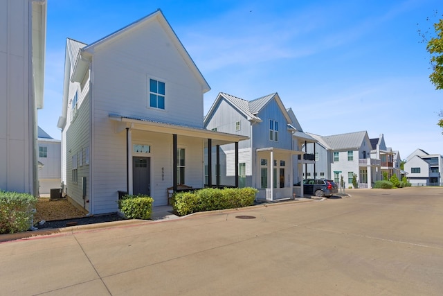 view of front of house featuring a porch, uncovered parking, central AC, a residential view, and metal roof