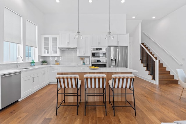 kitchen featuring a sink, under cabinet range hood, a center island, white cabinetry, and appliances with stainless steel finishes