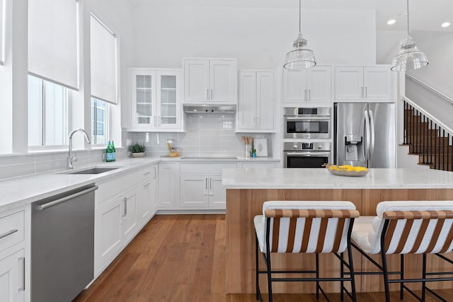 kitchen with a sink, under cabinet range hood, backsplash, appliances with stainless steel finishes, and a breakfast bar area