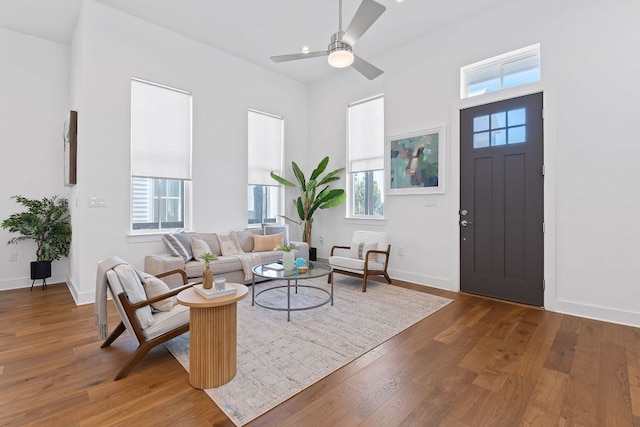 living area featuring baseboards, hardwood / wood-style floors, and a ceiling fan