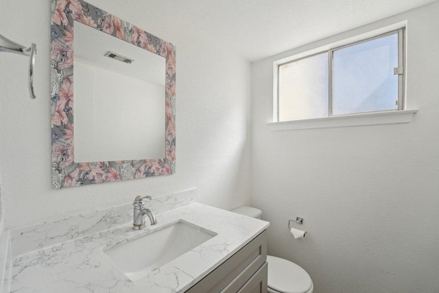 bathroom featuring vanity, toilet, a textured wall, and visible vents