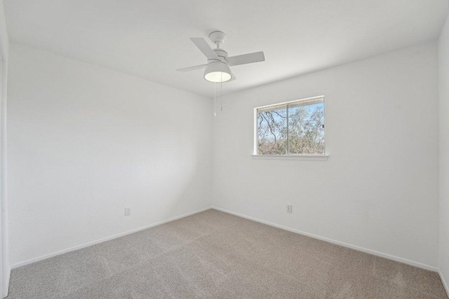 carpeted spare room featuring a ceiling fan and baseboards