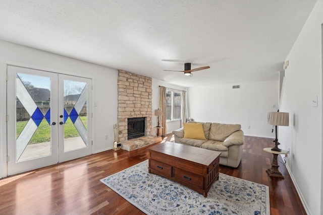 living room featuring a stone fireplace, visible vents, dark wood-style flooring, and a textured ceiling